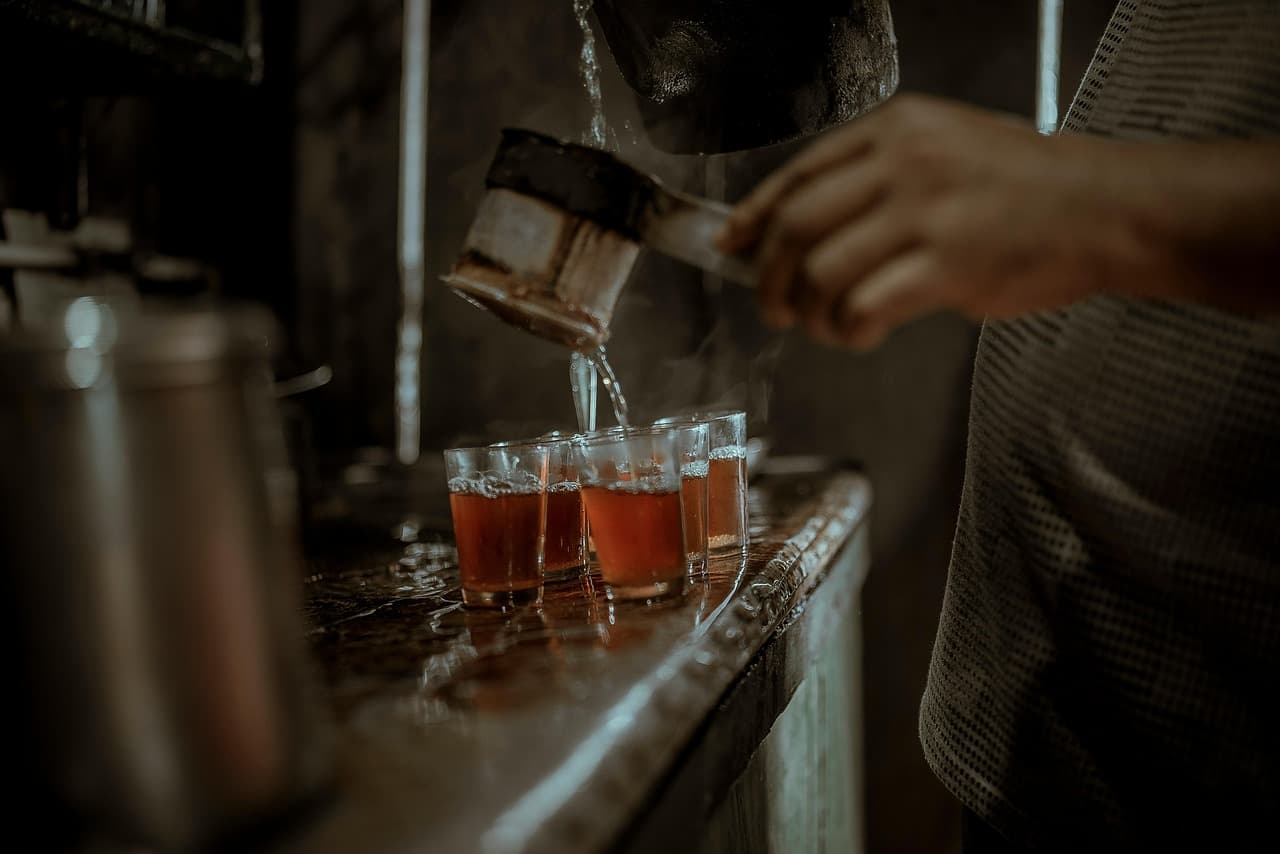 Tea poured from a pan into a row of glasses